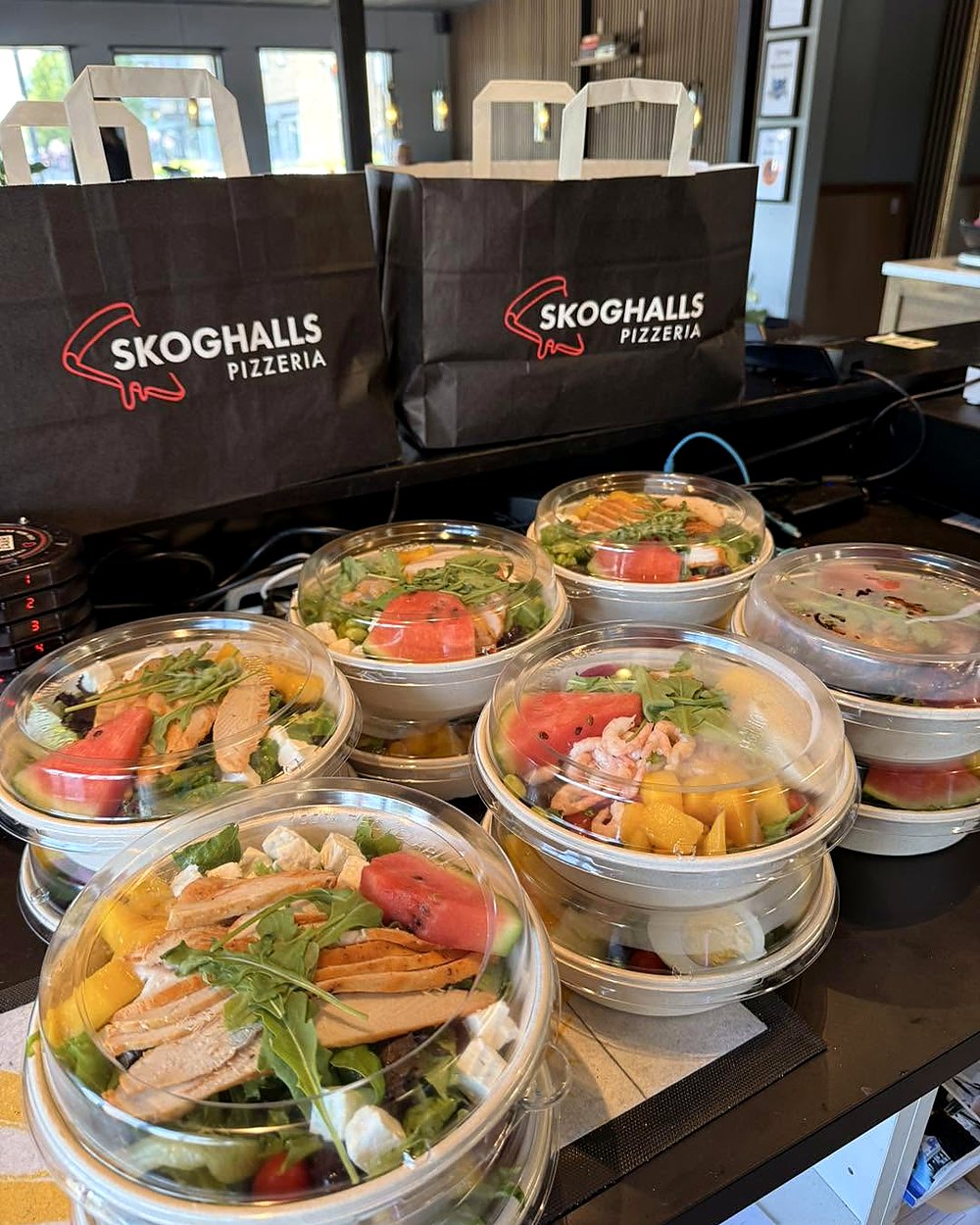 Salladsboxar med kyckling, räkor, mango och vattenmelon framför två Skoghalls-påsar